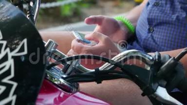 坐在复古摩托车上的男人在公园里用电话，时髦的概念。手的特写。3840x2160